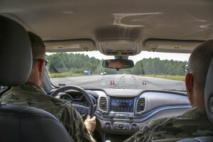 Two soldiers drive in a car on a course with cones on the road.