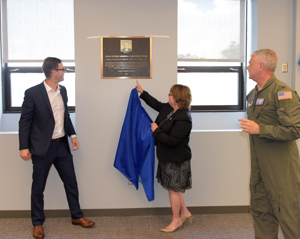 Marcy and Matt Steiner unveil the "Chuck Steiner Memorial Conference Room" plaque in the 109th Airlift Wing's new wing conference room at Stratton Air National Guard Base, Scotia, New York, as Col. Shawn Clouthier, 109th AW commander, looks on during a dedication ceremony to Chuck Steiner on Aug. 4, 2017. (U.S. Air National Guard photo by Senior Master Sgt. William Gizara/Released)