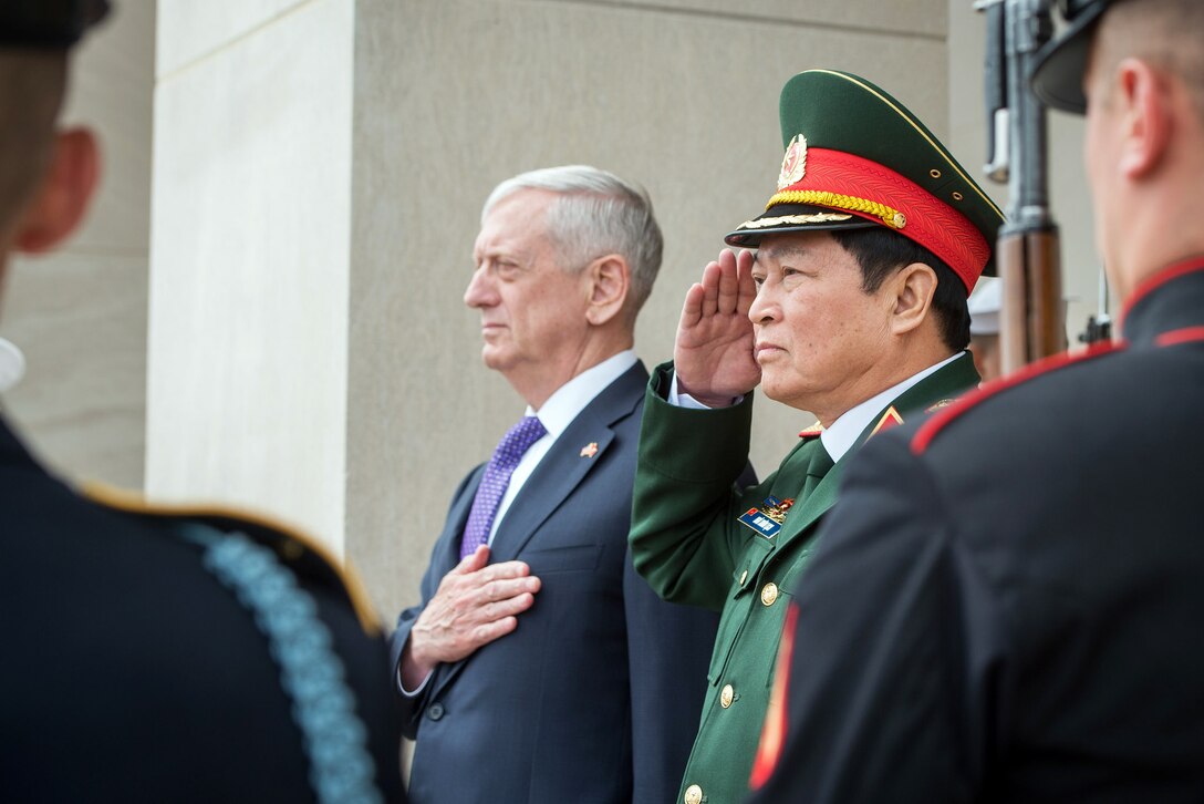 The Defense Secretary and a foreign military figure render honors during the national anthem.