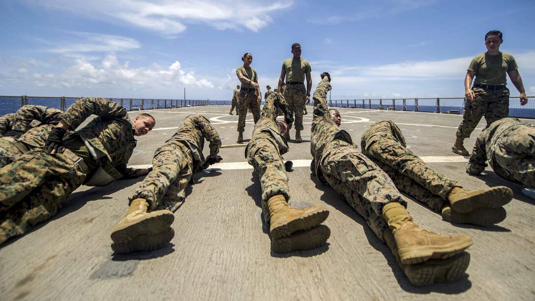 Marines lie in a row on a ship's flight deck while doing physical training.