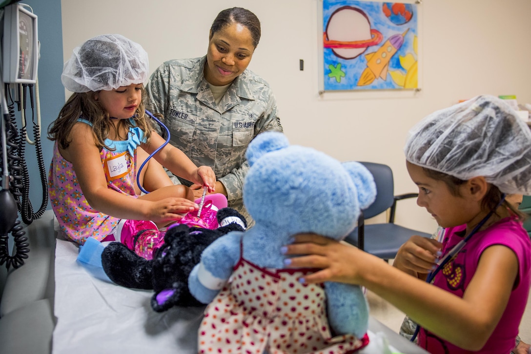 Two girls wearing hair nets tend to teddy bears as an airman watches.