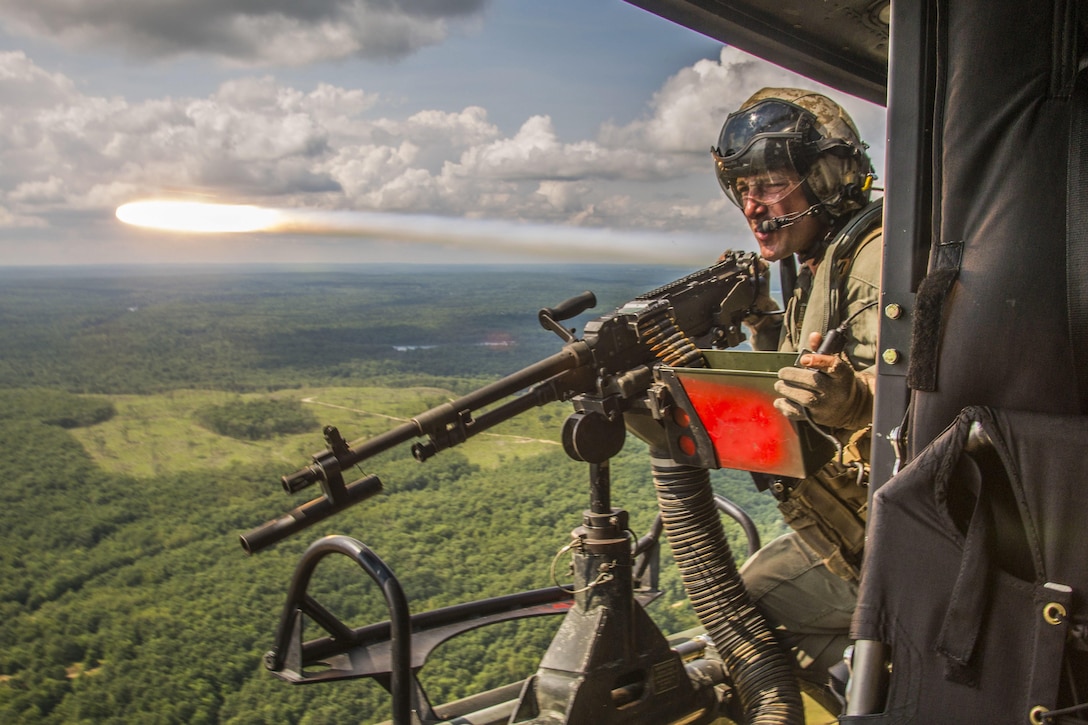 A flare shoots by a Marine manning a machine gun aboard an in-flight aircraft.