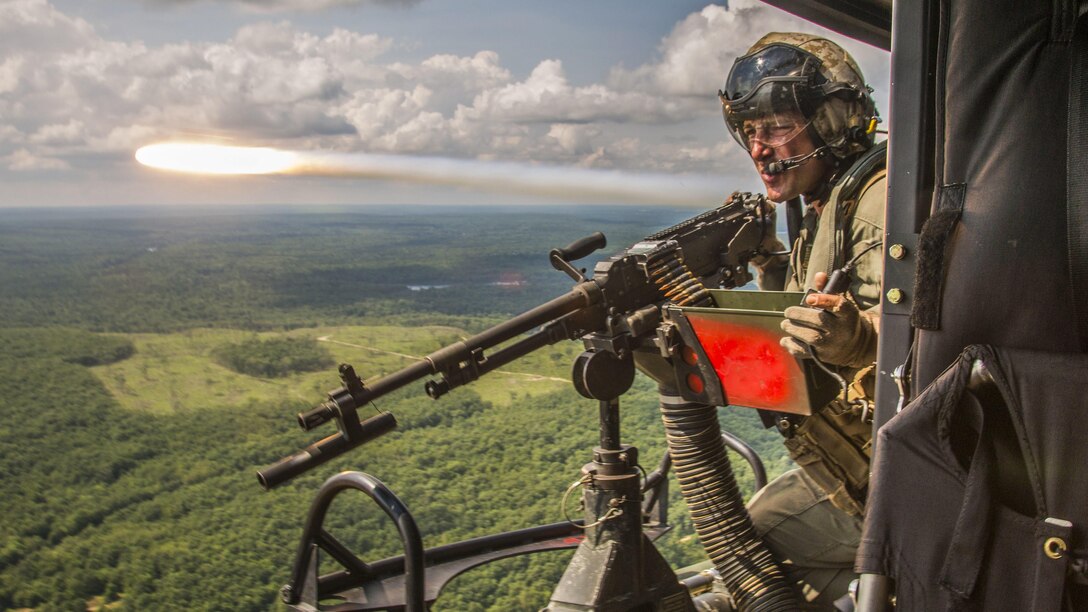 A flare shoots by a Marine manning a machine gun aboard an in-flight aircraft.