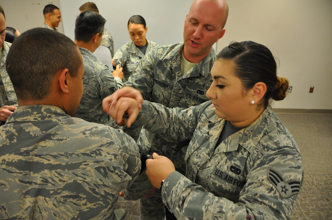 Senior Airman Antonia West, 302nd Logistics Readiness Squadron, simulates how to apply a combat tourniquet Senior Airman Adrian White, also with the 302nd LRS, while 302nd Aeromedical Staging Squadron personnel observe as part of pre-deployment training at Peterson Air Force Base, Colo., July 16, 2017.