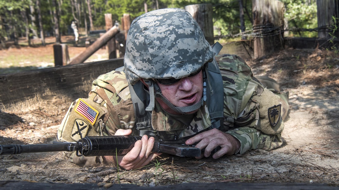 A soldier low-crawls with a weapon.