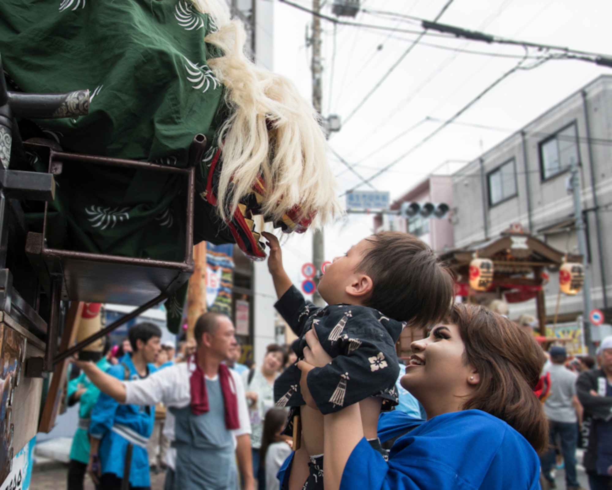Airman 1st Class Theresa Arzate holds a local child for Shishimai’s bite