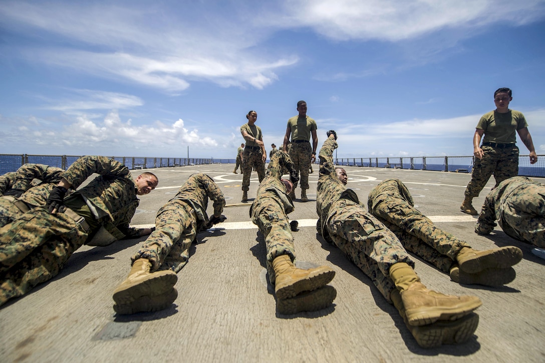 Marines lie in a row on a ship's flight deck while doing physical training.