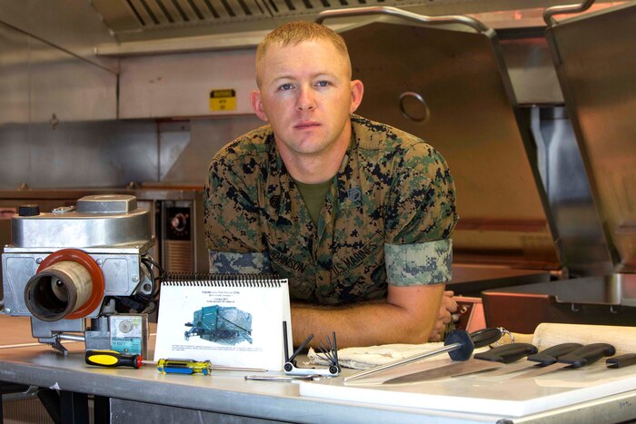 This image shows a Marine posing in a kitchen next to kitchen equipment.