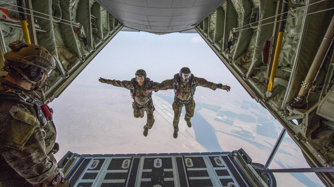 Two airmen are suspended side-by-side in the air, framed by the opening of the aircraft from which they jumped.