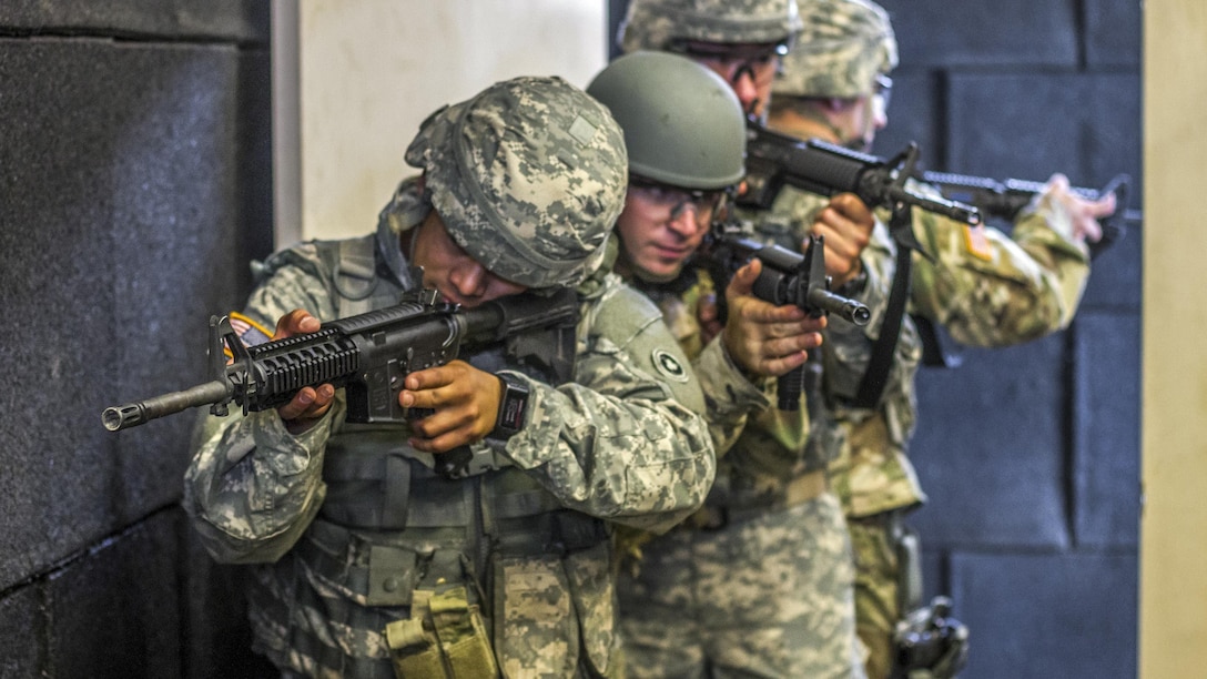 Soldiers aim weapons while moving in formation.