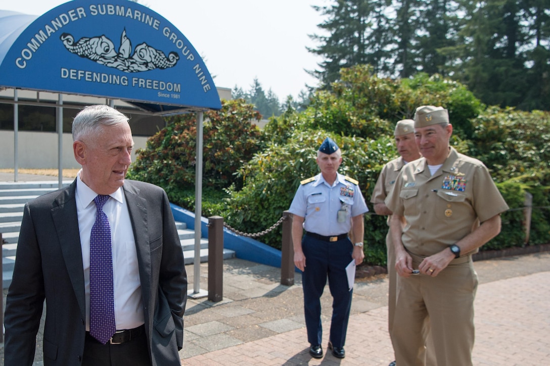 Defense Secretary Jim Mattis stands outside with Navy personnel.