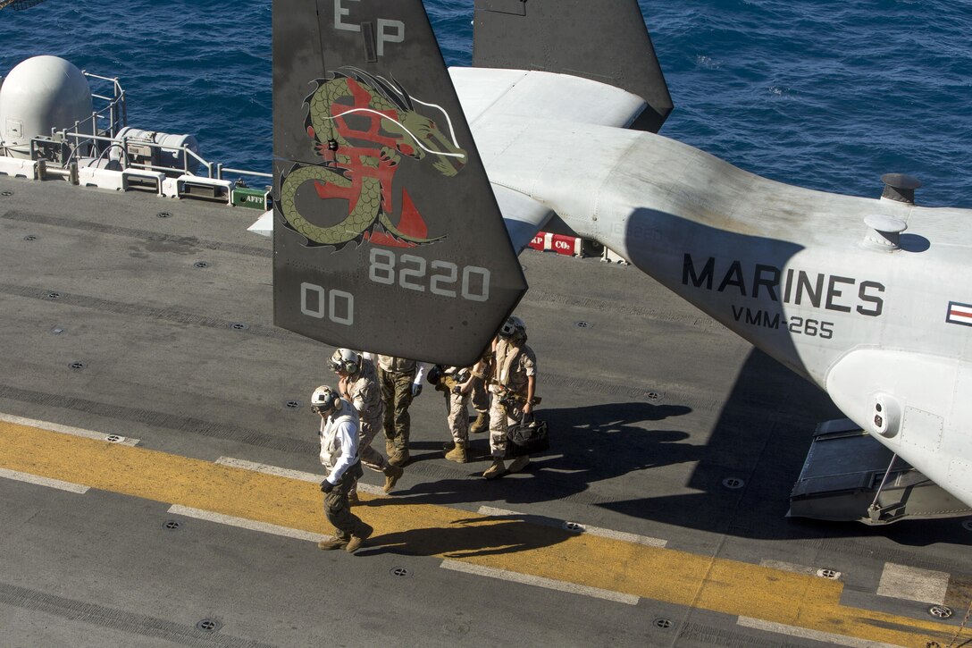 Service members walk on a ship's flight deck near a tiltrotor aircraft.