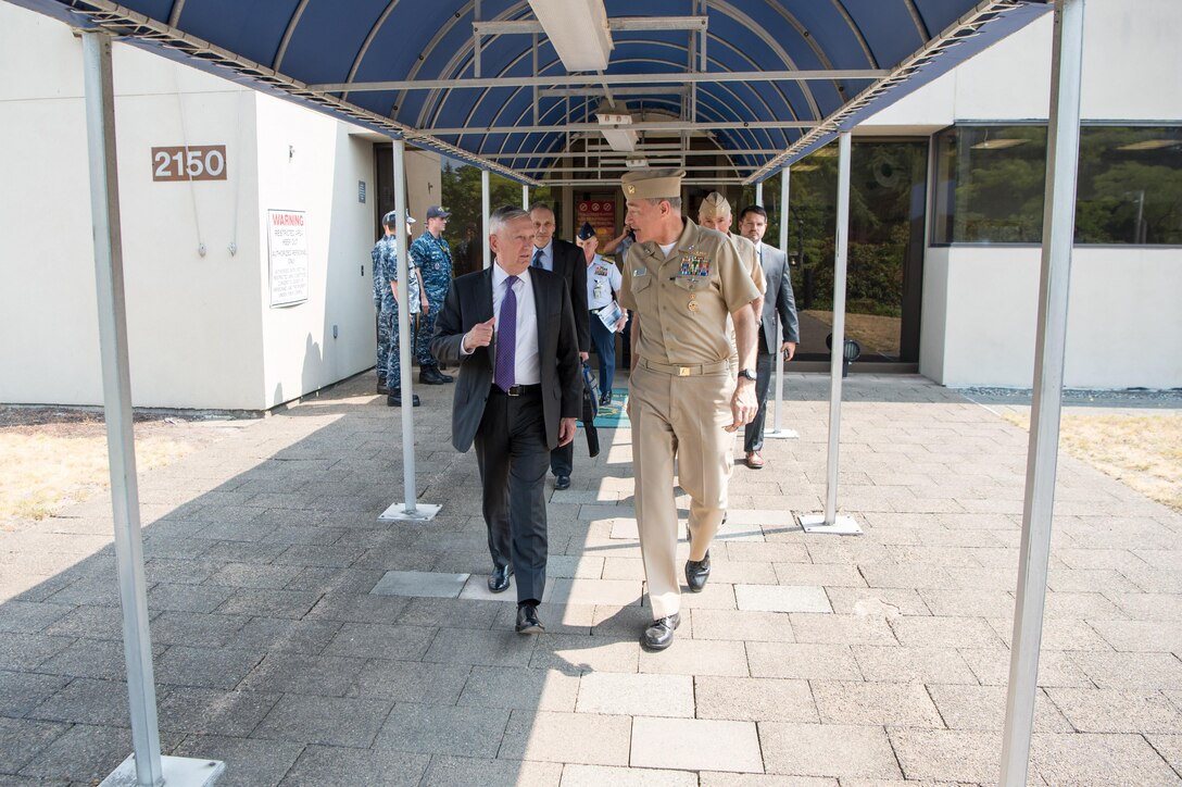 Defense Secretary Jim Mattis walks outside a building with military personnel.