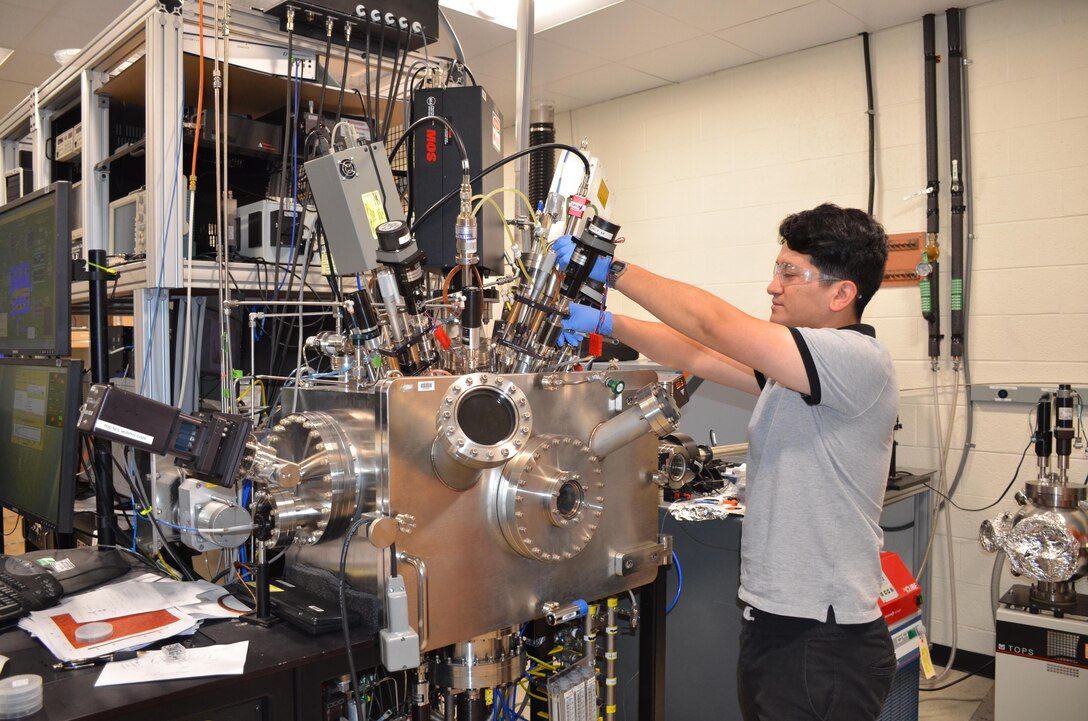 Graduate student from the University of Texas El Paso, Cristian Orozco, works in the Materials and Manufacturing Directorate over the summer. One of his duties includes working with a vacuum chamber for thin film coatings for optics.  (U.S. Air Force photo / Marisa Alia-Novobilski)