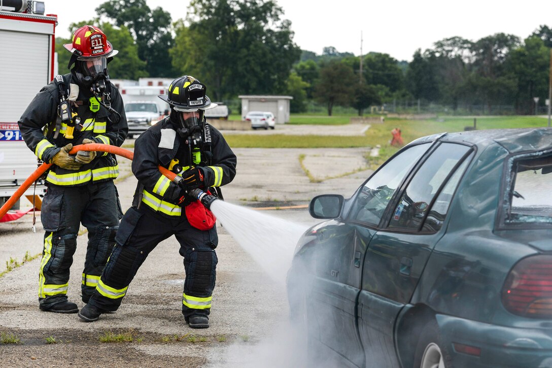 Firefighters hose down a car.