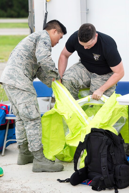 An airman helps a first responder don a protective suit.