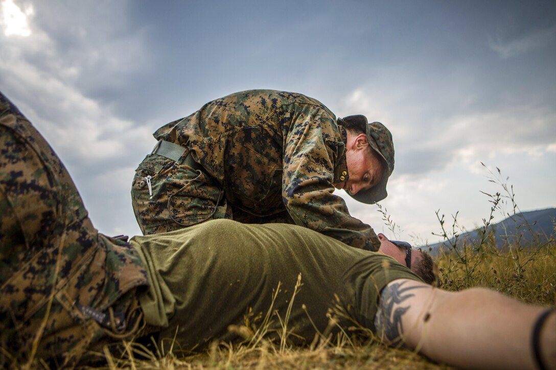 A Marine examines a fellow Marine lying on the ground