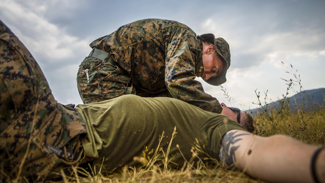 A Marine examines a fellow Marine lying on the ground.