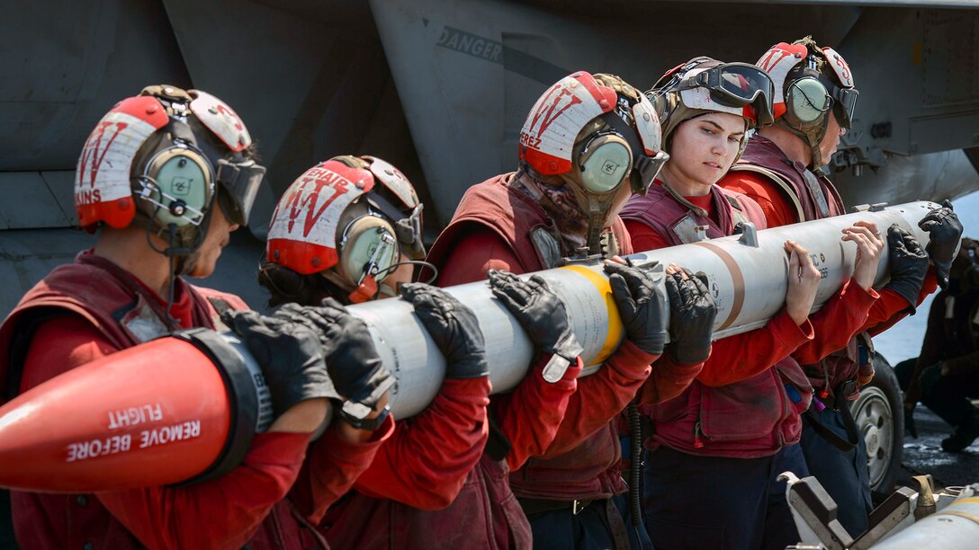 Sailors carry a missile on a ship.