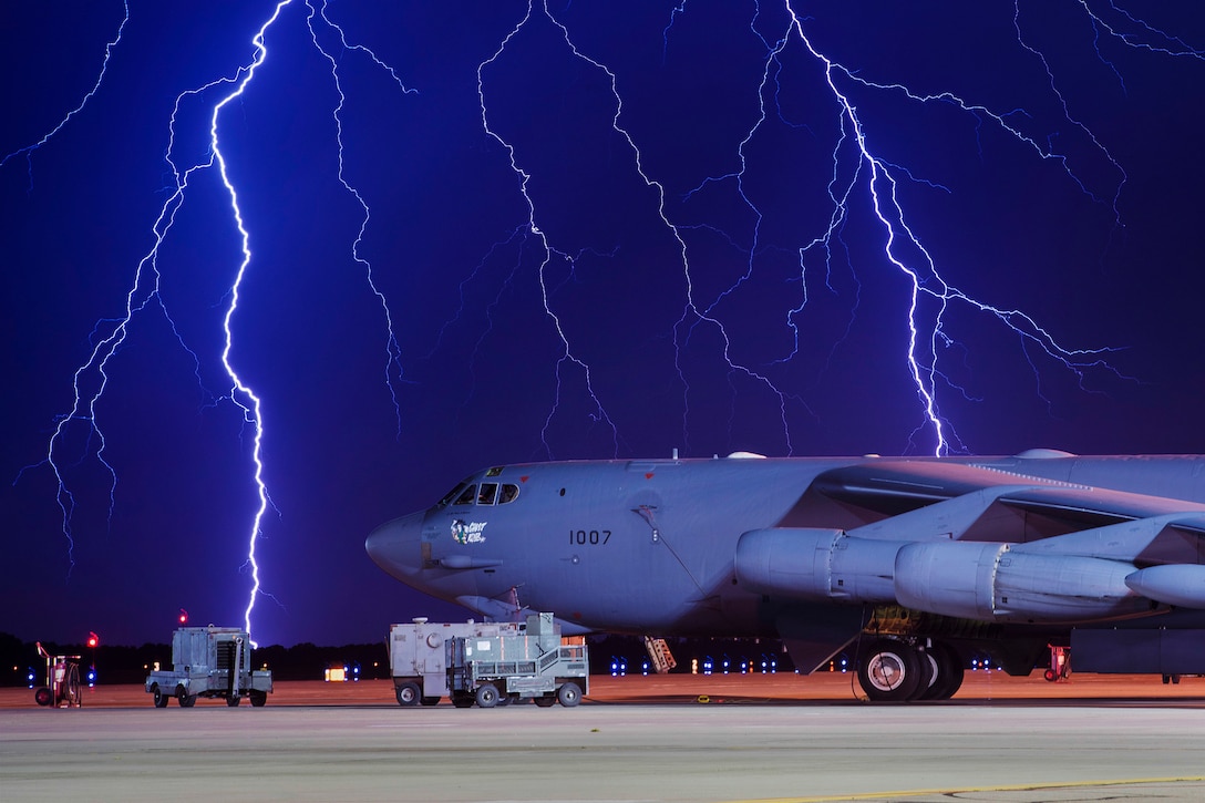 Lightning strikes behind an aircraft on a flight line.