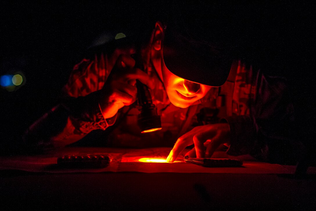 A soldier uses a flashlight to look at points on a map.