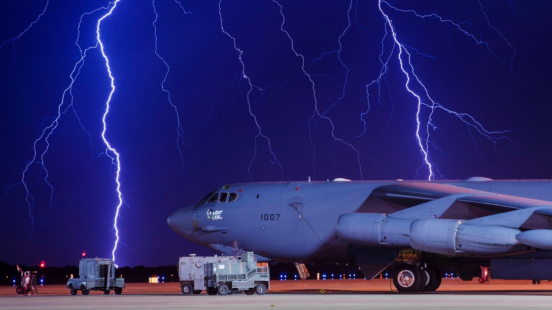 Lightning strikes behind an aircraft on a flight line.