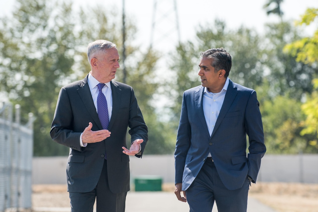 Defense Secretary Jim Mattis walks and talks with a person outside.