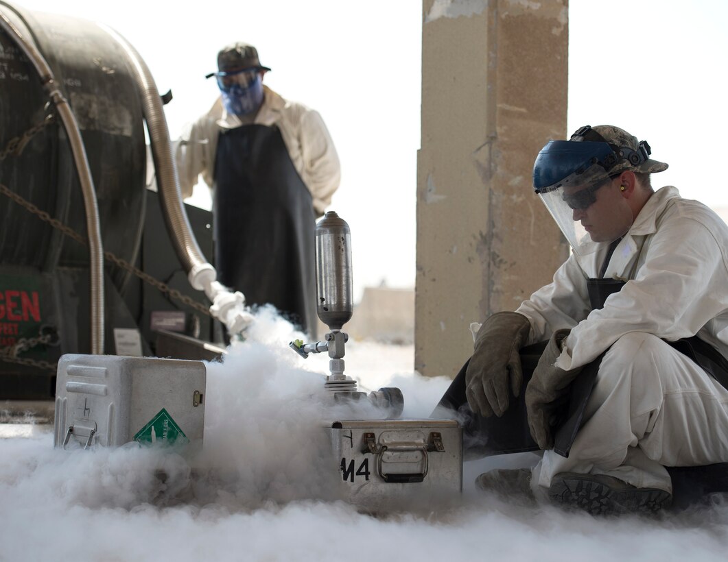 U.S. Air Force Staff Sgt. Kennie Delmo, left, a cryogenics supervisor and Senior Airman Samuel Fallot, a cryogenics journeyman with the 379th Expeditionary Logistics Readiness Squadron, Fuels Management Flight, fill a cryogenics sampler at Al Udeid Air Base, Qatar, Aug. 9, 2017.