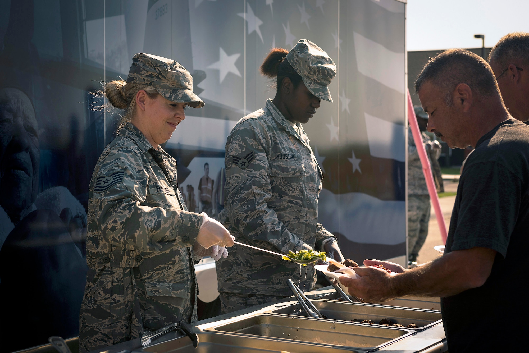 U.S. Air Force Tech. Sgt. Montana Fleissner, left, a services specialist with the 107th Force Support Squadron, New York Air National Guard, and Senior Airman Maya Houston, a services specialist with the 182nd Force Support Squadron, Illinois Air National Guard, serve dinner in Crow Agency, Mont., Aug. 1, 2017. They and six other services specialists provided meal support to 182nd Civil Engineer Squadron Airmen building veterans’ homes for the Innovative Readiness Training program. (U.S. Air National Guard photo by Tech. Sgt. Lealan Buehrer)