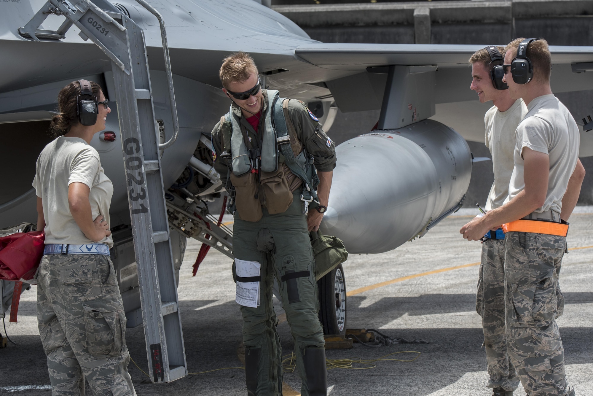 Three maintenance airmen talk with pilot next to an F-16 aircraft