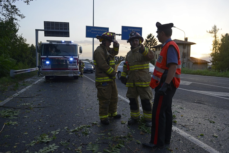 Aviano Air Base firefighters and a Carabinieri military police officer discuss removing a tree from a highway Aug. 10, 2017, in Pordenone Province, Italy. The 31st CES firefighters teamed with local first responders to clear roadways after heavy thunderstorms passed through the area. (U.S. Air Force photo by Tech. Sgt. Andrew Satran)