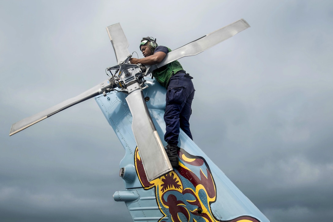 A sailor works on a helicopter's tail rotor.