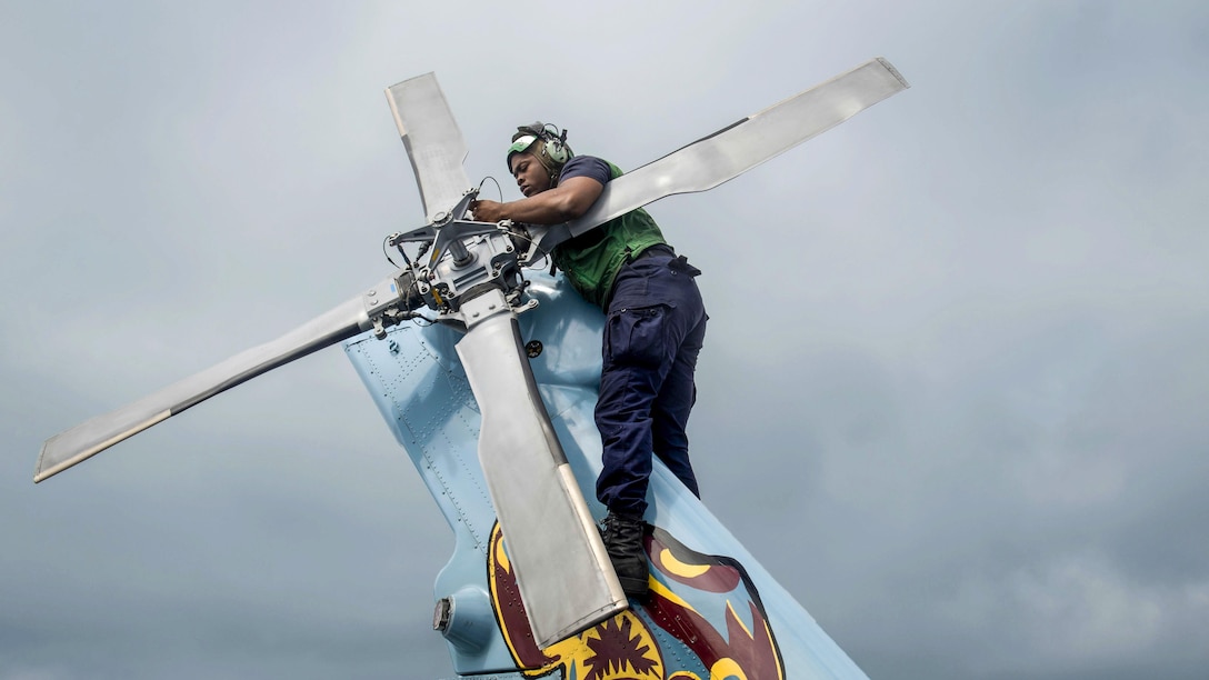 A sailor works on a helicopter's tail rotor.