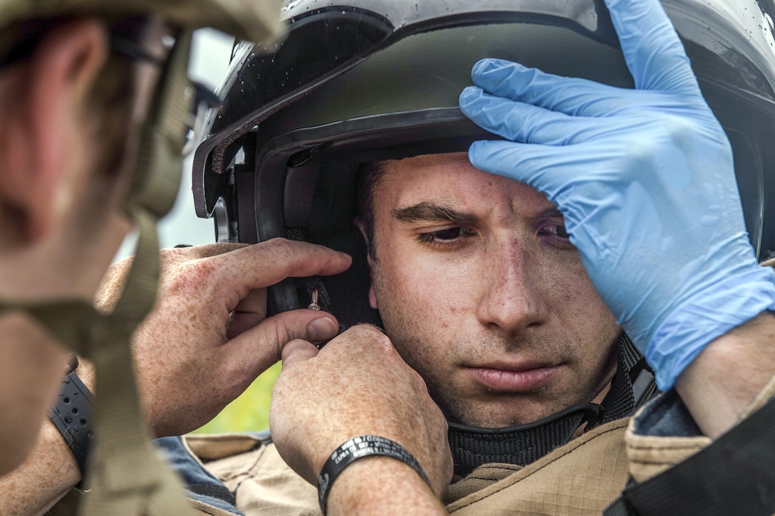 An airman his helmet on his head as a fellow airman helps him adjust it.