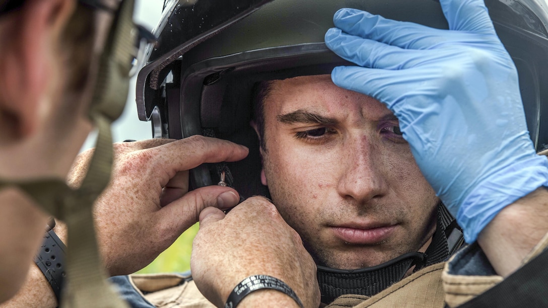 An airman his helmet on his head as a fellow airman helps him adjust it.