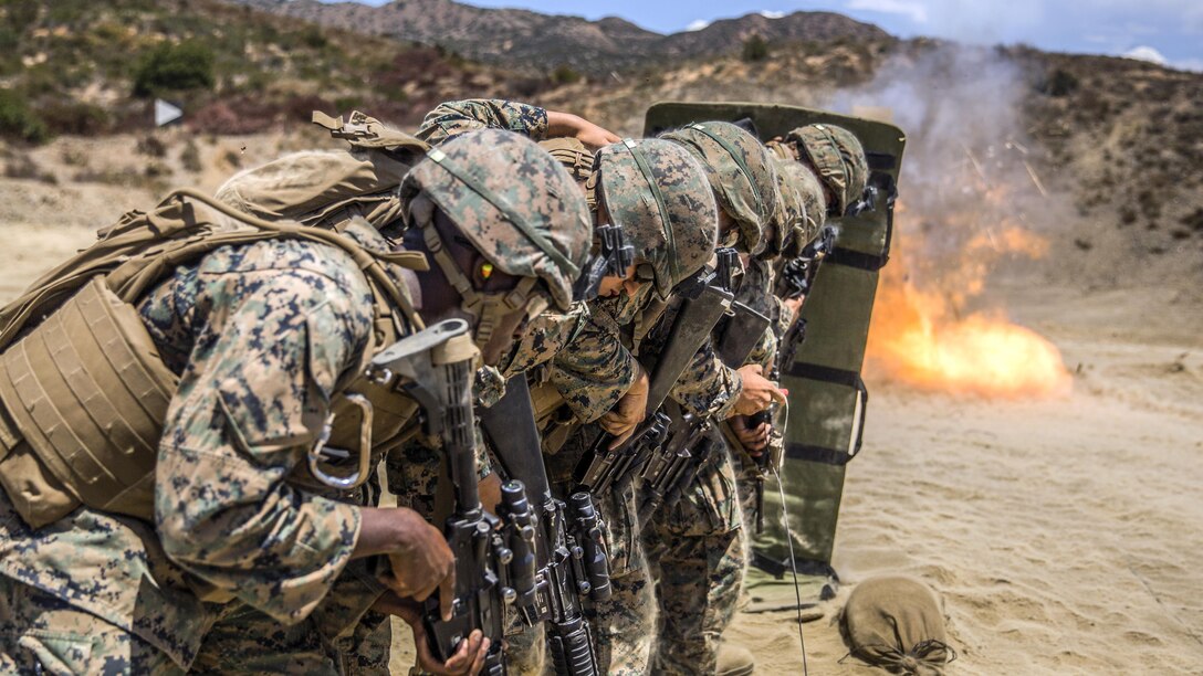 Marines line up behind a shield during a detonation.