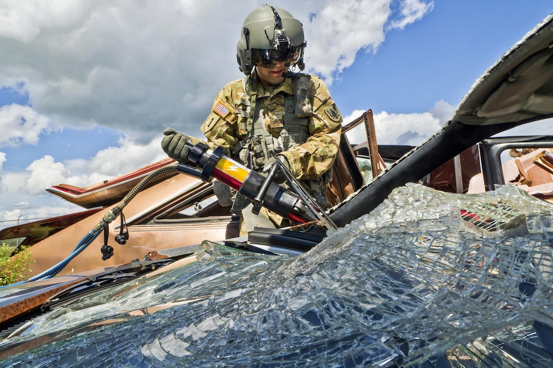 A soldier uses a cutting instrument on a broken window on a vehicle.