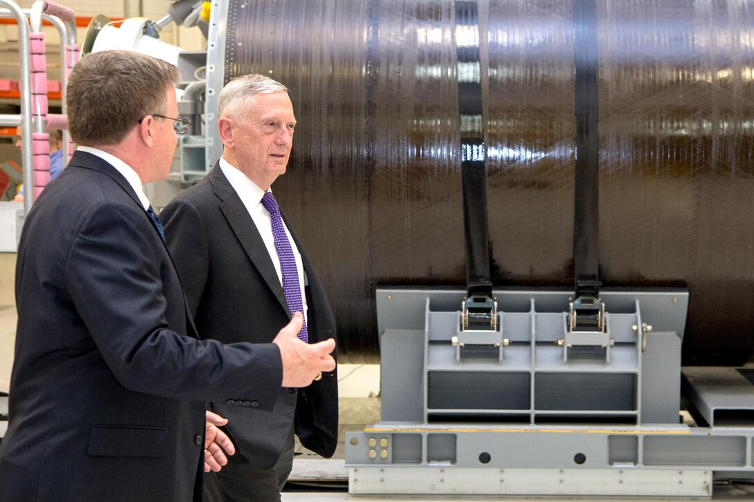 Defense Secretary Jim Mattis walks and talks with a person inside a building.