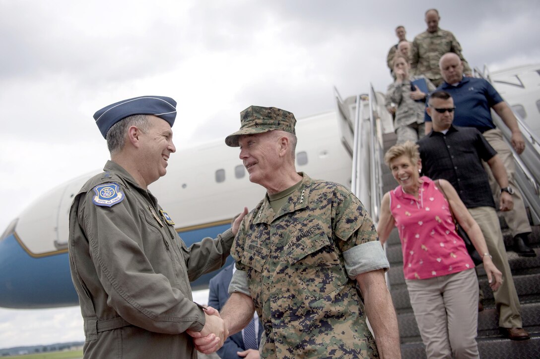 An Air Force officer and a Marine Corps officer shake hands outside of a plane.