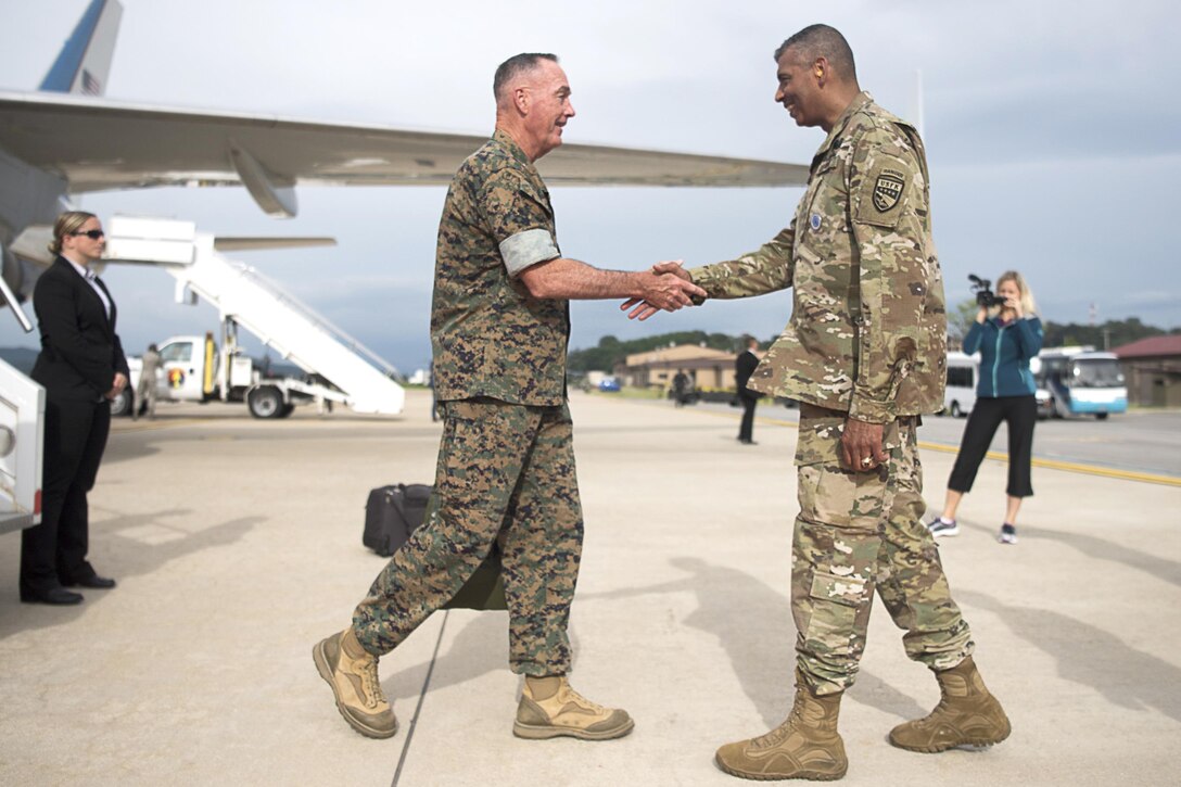 A Marine Corps officer and an Army officer shake hands on an airplane runway.