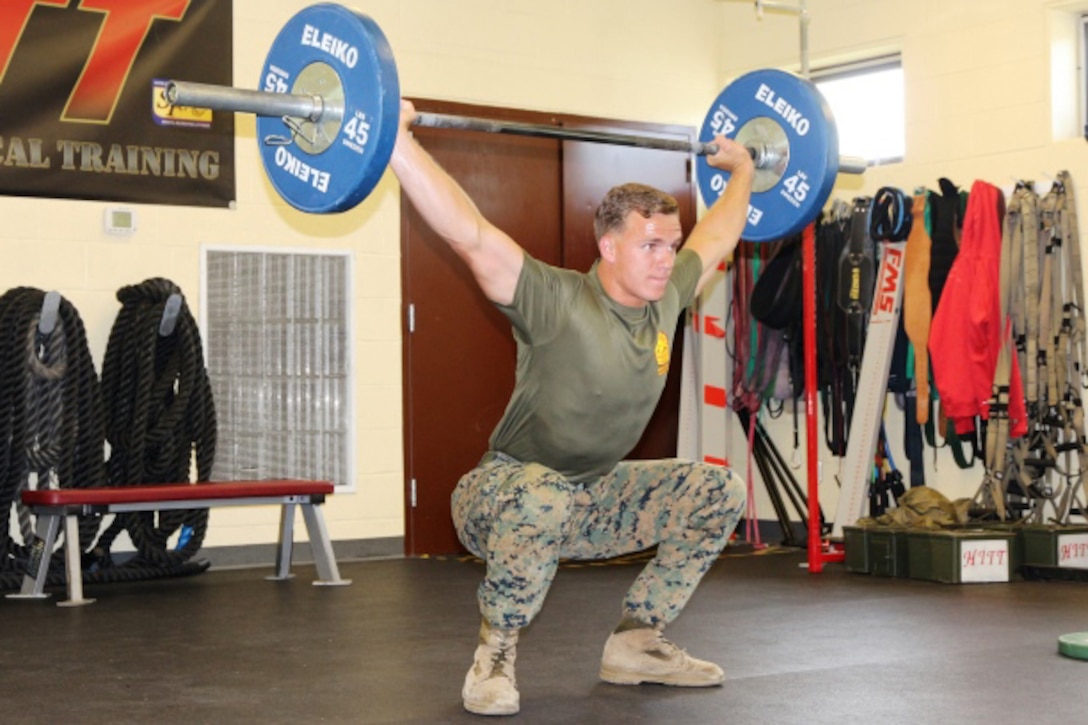 A Marine lifts a barbell at a gym.