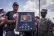 Master Sgt. Trae Clark, 27th Special Operations Wing Protocol superintendent, presents Calvin Fullerton, Clovis High School head football coach, with a plaque containing a flag flown over combat zones. After the death of Maj. Andrew Becker, Fullerton stepped in to help Clark through his rough time without knowing who he was. Clark felt that the good deed needed to be repaid. (U.S. Air Force Photo by Staff Sgt. Charles Dickens/Released)