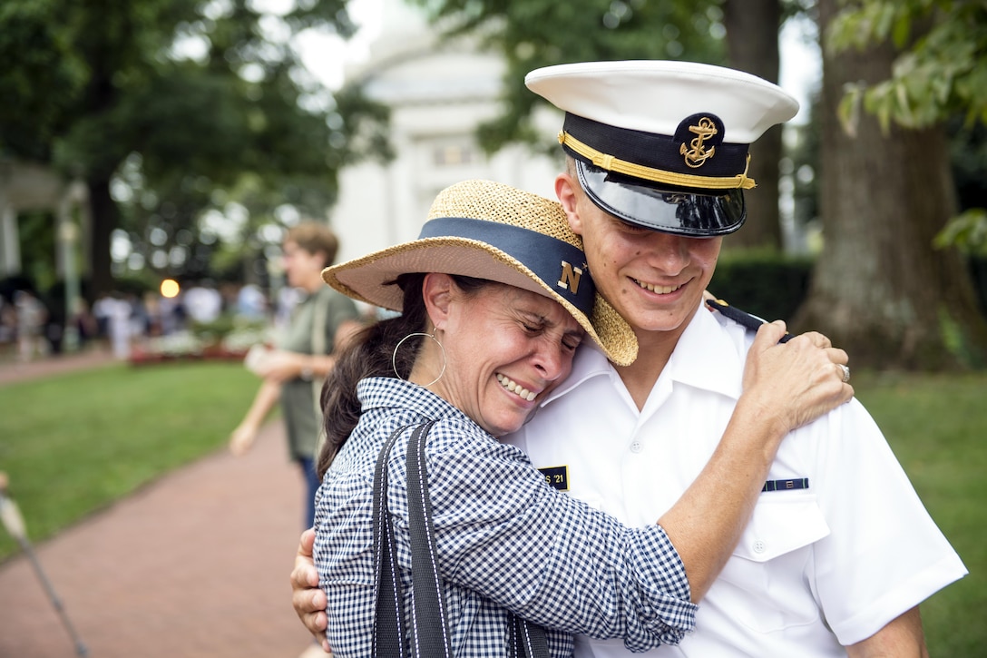A mother and her midshipman son smile and embrace each other on the U.S. Naval Academy's campus.