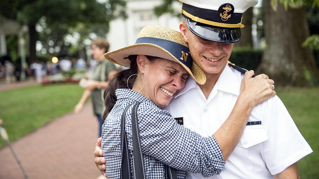 A mother and her midshipman son smile and embrace each other on the U.S. Naval Academy's campus.