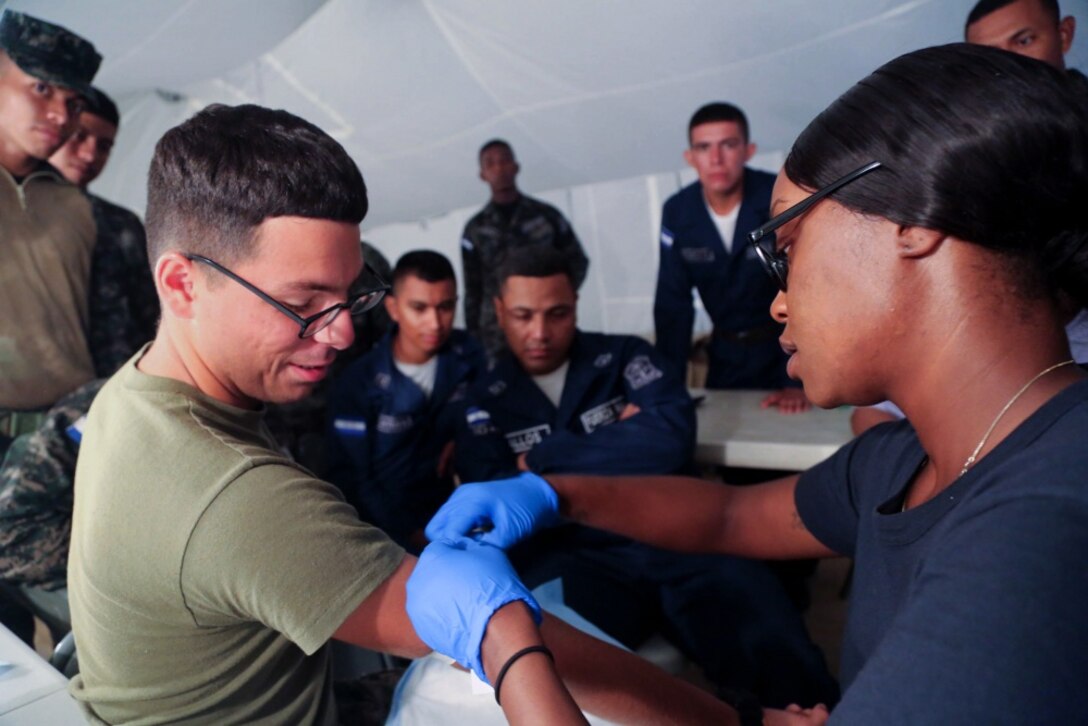 A U.S. Navy Hospital Corpsman prepares to take a blood sample from a U.S. Marine as Honduran troops look on.