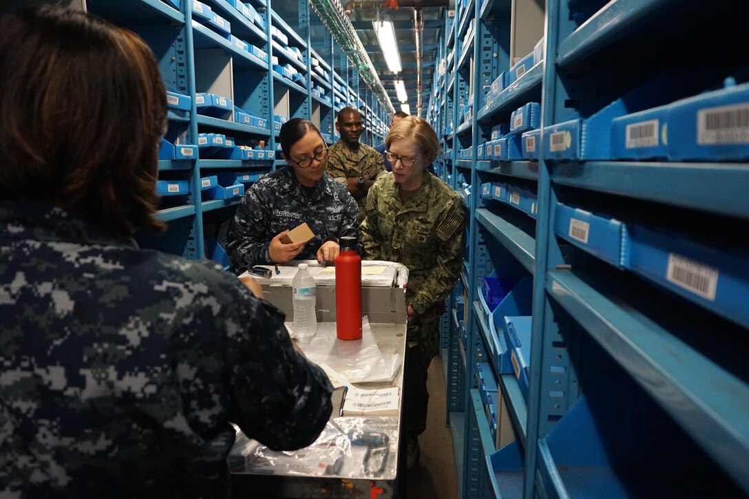 Navy Logistics Specialist 2nd Class Elsa Cervantes is demonstrating the process of picking bin materiel to DLA Joint Reserve Force director Navy Rear Adm. Deborah Haven.