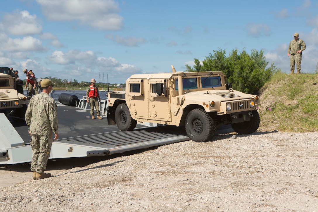 Sailors signal a landing craft to land on a beach to conduct lighterage during a maritime prepositioning force exercise at Blount Island, Fla., Aug. 13, 2017