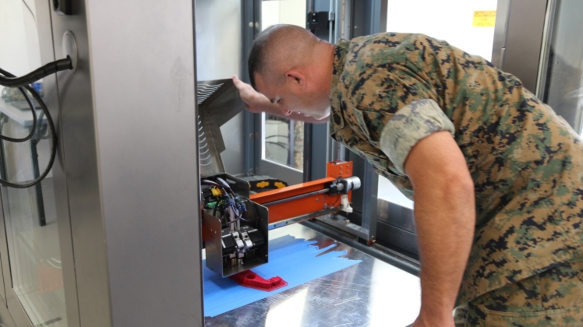 Gunnery Sgt. Doug McCue, a machinist with the 2nd Maintenance Battalion at Camp Lejeune, North Carolina, demonstrates the capabilities of a large-build 3-D printer in the X-FAB Facility Aug. 1. The X-FAB, or Expeditionary Fabrication, Facility is a self-contained, transportable additive manufacturing lab comprised of a 20-by-20-foot shelter, 3-D printers, a scanner and computer-aided design software system that can be used to fabricate repair and replacement parts in the field. (U.S. Marine Corps photo by Kaitlin Kelly)