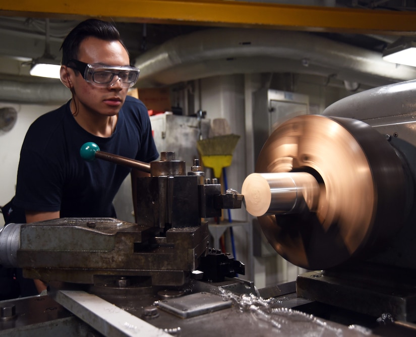 Navy Petty Officer 3rd Class Kody Kratz uses a lathe to turn down an aluminum carbide turning tube aboard the aircraft carrier USS George H.W. Bush
