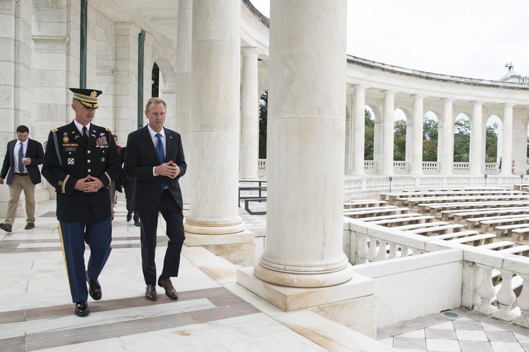 Deputy Defense Secretary Pat Shanahan walks with Army Col. Jason Garkey next to large pillars at Memorial Arena.